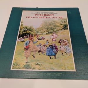 May include: A vintage vinyl record album featuring the soundtrack from the Royal Ballet film, "Peter Rabbit and Tales of Beatrix Potter." The cover art depicts a scene with costumed characters in a field. The album is in a dark green sleeve.