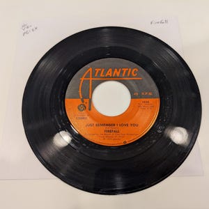 May include: A white ceramic mug with a black handle and the text "But First, Coffee" in a black, handwritten-style font. The mug is on a white surface.