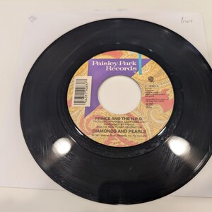 May include: A black vinyl record with a purple and gold label. The label says "Paisley Park Records" and "Prince and the N.P.G. Diamonds and Pearls".