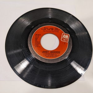 May include: A black vinyl record with a red and white label. The label says "Janet Jackson" and "What Have You Done For Me Lately".