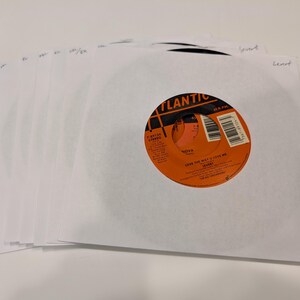 May include: A stack of white paper record sleeves with an orange vinyl record on top. The record label is orange and black and says "Atlantic" and "Nova" with the song title "Give the Right to Love Me" by "S.O.S. Band".