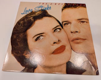 May include: Vintage vinyl record album cover featuring a woman and a man. The album title "Love Stinks" is in blue script. The J. Geils Band is printed at the top. The woman has red lipstick and the man has a serious expression.