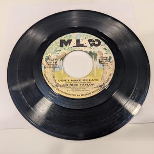 May include: A black vinyl record with a label that says "Don't Make Me Late" by Johnnie Taylor. The label also includes the record label "Malaco" and the song's producer, "George Jackson".