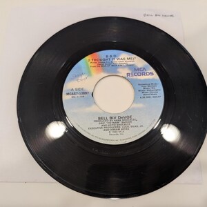 May include: A black vinyl record with a white center label featuring the text "B.B.D. (I THOUGHT IT WAS ME?)" and "BELL BIV DeVOE." The record is labeled "A SIDE" and includes the MCA Records logo. The record is on a white surface.