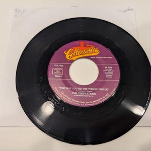 May include: A black vinyl record with a purple and yellow label. The label reads "Collectables" and features the text "THE WAY YOU DO THE THINGS YOU DO" by The Temptations. The record is in a white paper sleeve.