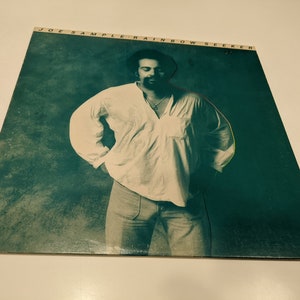 May include: A vintage vinyl record album cover featuring a man in a white shirt and blue jeans. The album title is "Joe Sample Rainbow Seeker".