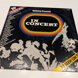 May include: Vintage vinyl record album cover for "In Concert" by various artists. The cover is black with a colorful rainbow-striped oval design and the text "IN CONCERT". The album features 20 original hits and artists. The cover also has the text "AS SEEN ON TV".