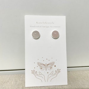Peut inclure: Une paire de boucles d'oreilles délicates avec une pierre rose clair sertie dans un cadre argenté. Les boucles d'oreilles sont présentées sur une carte blanche avec le texte "Katelifestyle Handcrafted Antique Accessories".