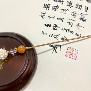 May include: A gold hair stick with a white pearl cluster, a clear crystal bead, and a brown agate bead.