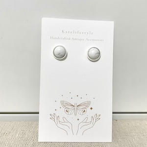 May include: A pair of white marble stud earrings on a white card with the text "Katelifestyle Handcrafted Antique Accessories" and a drawing of a hand holding a butterfly.