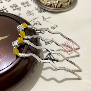 Può includere: Tre pettini per capelli in argento con perline gialle e accenti di fiori argentati. I pettini sono su una superficie di legno marrone.