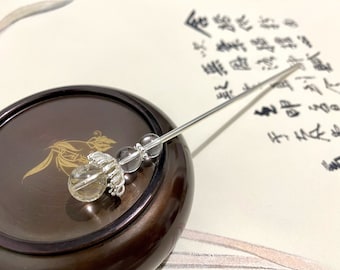 May include: A silver hair stick with a clear quartz crystal and two smoky quartz beads. The stick is resting on a wooden surface.