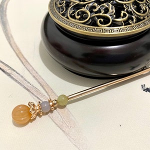 Op de afbeelding: Een gouden en bruine wierookbrander met een decoratief deksel en een gouden en oranje kralen wierookstokje.