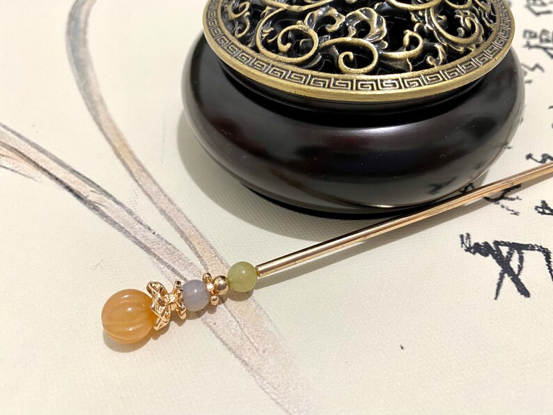 Op de afbeelding: Een gouden en bruine wierookbrander met een decoratief deksel en een gouden en oranje kralen wierookstokje.
