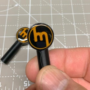 May include: Two black key fobs with a yellow and black logo. The logo is a stylized "M" inside a circle.