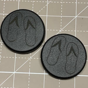 May include: Two black round coasters with a design of flip flops on each.