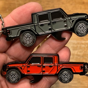 May include: Two metal Jeep keychains, one in black and one in red, with bottle opener features. Both keychains are in the shape of a Jeep Gladiator pickup truck.