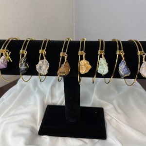 May include: Eight gold bangle bracelets with different colored crystal charms. The charms are wrapped in gold wire. One charm has a gold letter K.