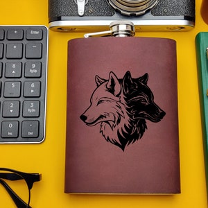 Pode incluir: Uma garrafa de couro marrom com uma silhueta preta de duas cabeças de lobo que se olham. A garrafa tem uma tampa prateada.