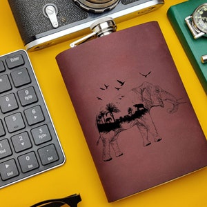 Puede incluir: Una petaca de cuero marrón con una tapa plateada y una ilustración en blanco y negro de un elefante con una escena de bosque dentro del elefante.