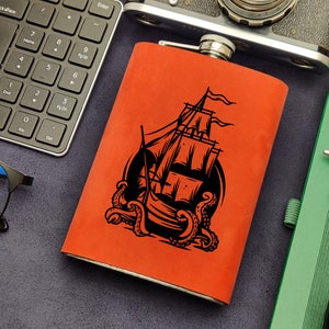 May include: A red leather flask with a black design of a ship being attacked by an octopus.