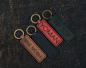 May include: Four leather keychains with gold rings. The keychains are brown, red, black, and green. The text on the keychains reads "Benz Mobile", "Yoman", "Tip Top", and "H.I.G."