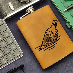 May include: A brown leather flask with a black design of a bottle with a message in the waves.