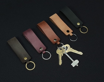 May include: Five leather keychains in different colors, including brown, tan, burgundy, black, and dark brown. Each keychain has a metal ring and a key attached.