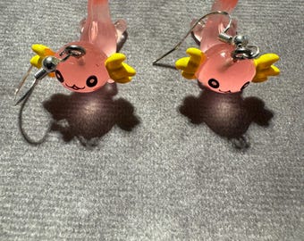 Peut inclure: Une paire de boucles d'oreilles en forme d'axolotl rose avec des branchies jaunes. Les boucles d'oreilles sont en résine et ont des crochets argentés.