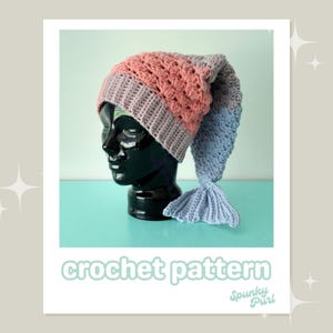 May include: A crochet pattern for a mermaid hat with a pink and gray hat and a blue tail. The hat is on a black mannequin head. The text "crochet pattern" is below the image and "Spunky Purl" is below the text.