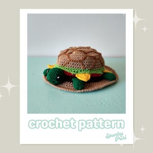 May include: Crochet pattern for a turtle-shaped hat with a brown, green, yellow, and red design. The hat is shaped like a hamburger bun with a green turtle head and legs.