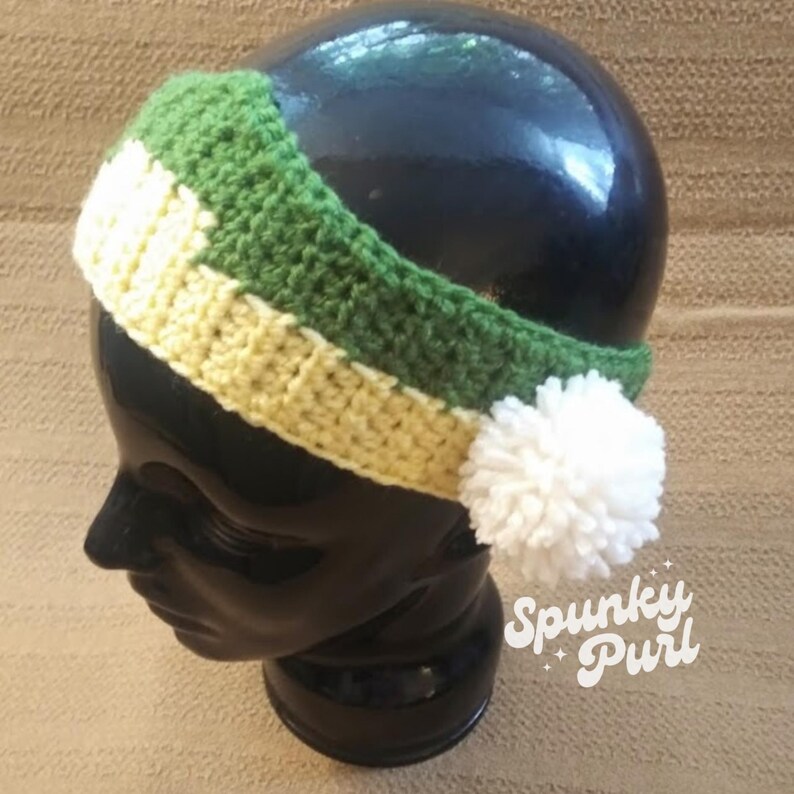 May include: A green, yellow, and white crocheted headband with a white pom-pom on the side. The headband is on a black mannequin head. The text "Spunky Purl" is visible in the lower right corner of the image.