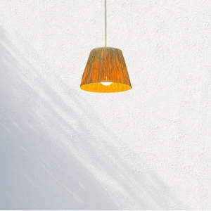 May include: A pendant light fixture with a conical lampshade. The lampshade is a warm orange color with a textured, woven appearance. The light fixture hangs from a white cord against a white wall.