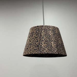 Può includere: Paralume con stampa leopardata. Il paralume è marrone scuro con macchie nere, sospeso da un cavo nero. Ha una forma conica, adatto per lampade a sospensione.