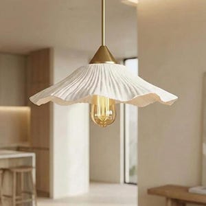 May include: A white, pleated pendant light fixture with a gold-colored stem and cone-shaped top. The light has a vintage-style bulb. The fixture is hanging in a room with neutral-colored walls and furniture.