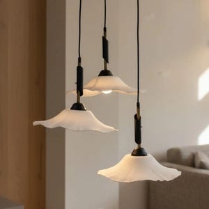 May include: A contemporary chandelier with three hanging lights. Each light has a white, petal-shaped shade, suspended from black cords and a circular black ceiling mount. The fixture has gold and black detailing.