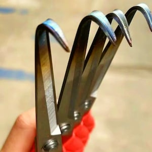 May include: Close-up of four metal hooks with blue and silver coloring. The hooks are curved and have a sharp point. The hooks are held in a hand.