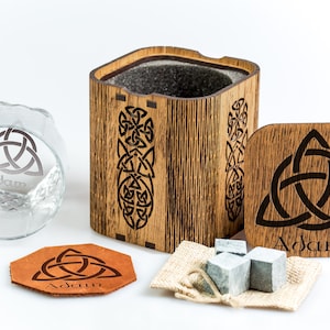 May include: A personalised whiskey gift set with a wooden box, a glass, a leather coaster, and a bag of whiskey stones. The box, glass, and coaster all feature a Celtic knot design and the name "Adam".
