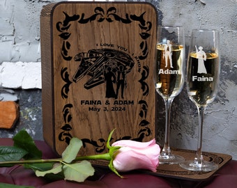 Può includere: Scatola di legno con un design inciso a laser di un'astronave di Star Wars e due figure. La scatola è decorata con un motivo floreale e il testo "Ti amo, lo so" e "Faina & Adam, 3 maggio 2024". Due flute da champagne sono incise con i nomi "Adam" e "Faina".