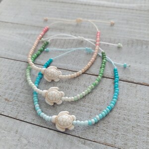 May include: Three layered bracelets with a gradient of colors, starting with pink, then green, and finally blue. Each bracelet has a white turtle charm.