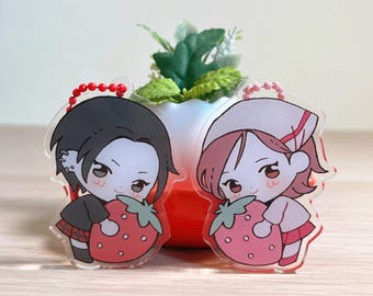 May include: Two acrylic keyrings with anime-style characters, each holding a large strawberry. One character has black hair and a dark outfit, the other has pink hair and a white and pink outfit. Both keyrings have red beaded chains.