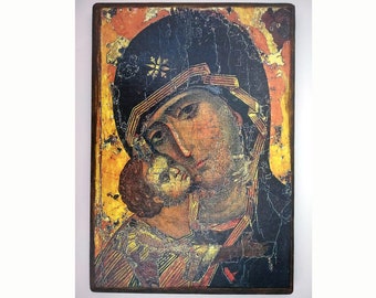 May include: A vintage-style icon depicting the Virgin Mary holding the baby Jesus. The icon is painted on a wooden panel with a dark brown frame. The Virgin Mary is wearing a blue robe with a gold trim and a red sash. The baby Jesus is wearing a white robe. The icon is in a distressed condition, with some of the paint flaking off.