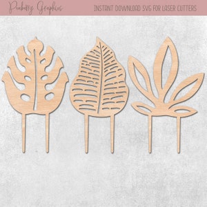 May include: Three wooden leaf shapes on sticks, perfect for cake toppers or craft projects. The leaves are in a natural wood color and have intricate designs.