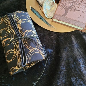 May include: A black fabric pouch with a gold pattern of circles and lines. The pouch is tied with a black cord and has a tassel.