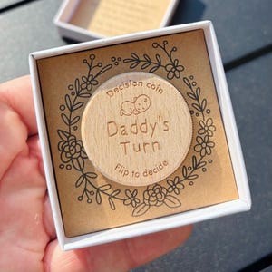 以下が含まれることがあります： 縁に花柄が施された木製の硬貨。コインには「Decision coin Daddy's Turn Flip to decide」と書いてあります。