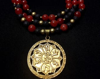 Könnte beinhalten: Eine mehrschichtige Halskette mit roten und schwarzen Perlen und goldfarbenen Akzenten. Der Anhänger ist ein goldfarbenes, kreisförmiges Design mit komplizierten Mustern und Symbolen. Die Halskette wird vor einem schwarzen Hintergrund präsentiert.