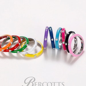 May include: A set of ten colourful enamel rings, each featuring a single clear stone. The rings are arranged in a rainbow pattern, with the colours orange, red, green, yellow, purple, blue, turquoise, pink, black, and white.