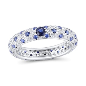 May include: A silver ring with a band adorned with small, round, white and blue gemstones. The ring has a prominent, dark blue gemstone at its centre. The gemstones are closely set, producing a sparkling appearance.