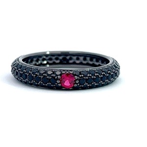 May include: Black band ring with a single red gemstone in the centre, surrounded by smaller black gemstones.