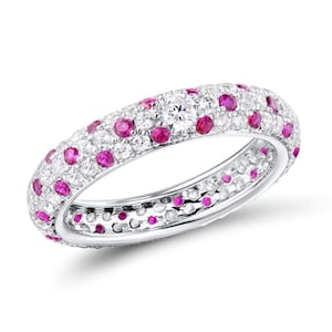 May include: A white gold ring set with white diamonds and pink rubies. The ring has a central diamond and is designed with multiple rows of gemstones. The ring is a continuous band.